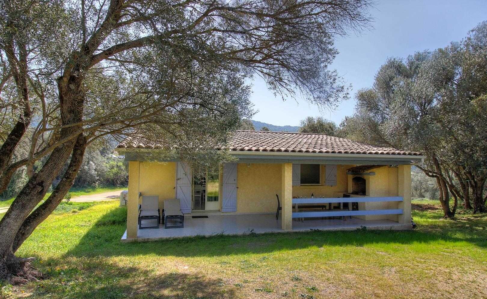 A small, single-story building with a tiled roof, a porch with two chairs, and a small table.