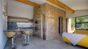 Uma cozinha moderna com parede em pedra, área de refeições com banquetas e um sofá amarelo.