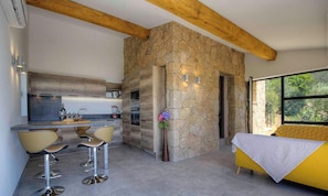 Eine moderne Küche mit einer Wand aus Stein, ein Essbereich mit Barhocker und ein gelbes Sofa.