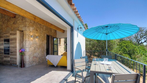 Um pátio com mesa e cadeiras, um guarda-sol azul e uma cama com cobertura branca.