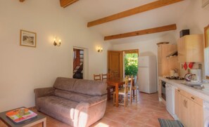 Ein gemütliches Wohnzimmer mit einer Couch, einem Esstisch mit Stühlen, einer Küche mit Holzschränken und Geräten sowie einer Treppe, die eine weitere Ebene hinaufführt.