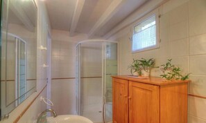 Ein Badezimmer mit Dusche, Waschbecken, einem Holzschrank und einem Fenster.
