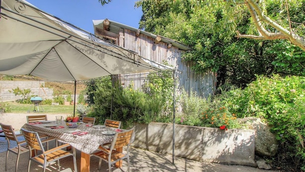 En udendørs terrasse med et spisebord, omgivet af stole og en stor parasol.