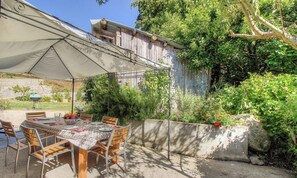 Eine Terrasse im Freien mit Esstisch und Stühlen, beschattet durch einen großen Sonnenschirm.