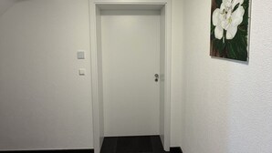 Un corridoio con una porta bianca, un tappeto nero e un quadro raffigurante un fiore bianco sulla parete.