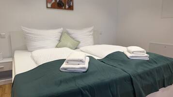 A double bed with white bedding and a green throw blanket, a nightstand with a lamp, and a wall art piece above the bed.