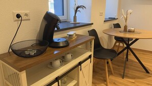 Un angolo cottura compatto con una macchina del caffè, un cesto e un tavolino con delle tazze.