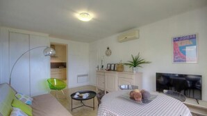 Ein Wohnzimmer mit einer Couch, einem kleinen Tisch mit Tablett, einem Fernseher und einem Poster an der Wand.
