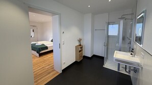 Un baño moderno con cabina de ducha de vidrio, un lavabo blanco y una mesita de noche de madera.