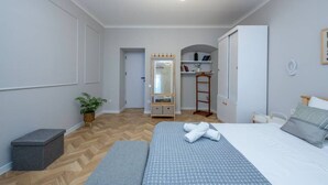 A bedroom with a bed, bedside table, bench, wardrobe, mirror, and a small plant.