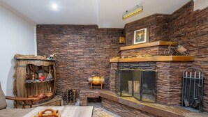 A room with a stone wall, a fireplace, a wooden shelf, and a woven basket.