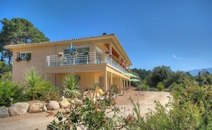 A two-story building with a balcony, outdoor seating, and a garden area. - Manon - LEVIE - Gîte (LEVIE)