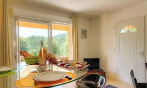 A room with a dining table set for a meal, a television, and a door leading outside. - Manon - LEVIE - Gîte (LEVIE)
