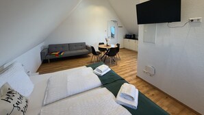 Una habitación con dos camas, un sofá, una mesa de comedor y un televisor montado en la pared.