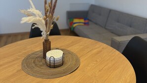 Una mesa de madera redonda con un mantel tejido, una pequeña maceta de cerámica blanca con una planta y un soporte decorativo de metal.