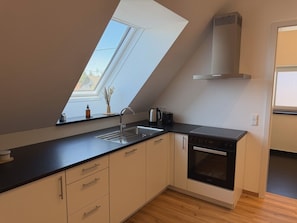 A kitchen with a skylight, a stove, a sink, and a window.