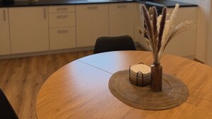 Una cocina moderna con tragaluz, una mesa redonda para comer con un mantel tejido y un jarrón con plantas secas.