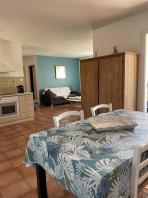 A kitchen with a stove, a dining table with chairs, a wooden wardrobe, and a sofa in the background. - Residence San Micheli 2 (SERRA DI FIUMORBU)