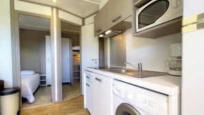 A compact kitchenette with a microwave, sink, and washing machine, a bed in the adjacent room, and a wooden floor. - Zonza, N°32 - GHISONACCIA (GHISONACCIA)