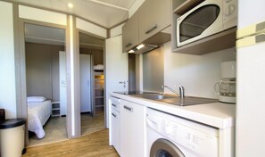 Eine kompakte Küchenzeile mit Mikrowelle, Spüle und Waschmaschine, ein Bett im angrenzenden Zimmer und Holzboden.