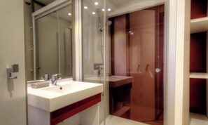Ein modernes Badezimmer mit einem weißen Waschbecken, einem Spiegel und einer Duschkabine aus Glas.