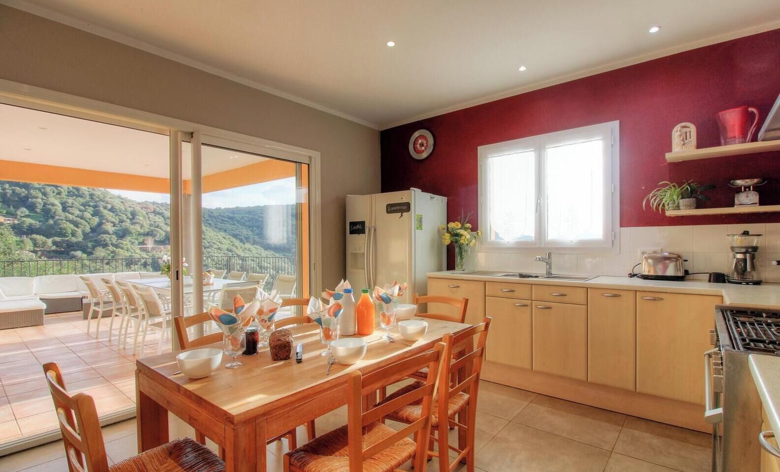 A modern kitchen with a dining area, large windows, and a view of the outdoors.