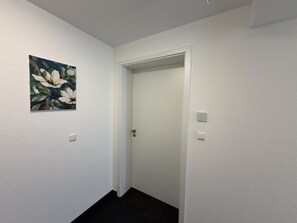 A narrow hallway with a white door, a light switch, and a painting on the wall.