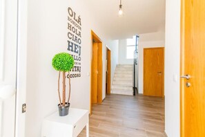 Ein Flur mit einer Topfpflanze, einer Wand mit mehrsprachigen 'HELLO'-Schildern und Holztüren.