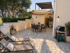 Un patio al aire libre con piso de piedra, una parrilla, una zona de estar y plantas en macetas.