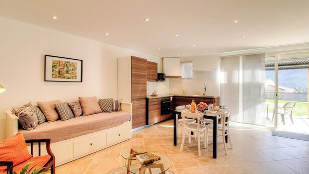 Ein modernes Wohnzimmer mit einer Couch, einem Esstisch, Stühlen, einer Küchenzeile und einer Glastür zum Außenbereich.