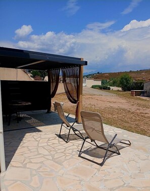 An outdoor patio with stone flooring, two chairs, a table, and a covered area with curtains. - Petra rossa - PERI - Guest house (PERI)