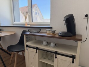 A kitchenette with a coffee maker, a bowl, and cups on a shelf.