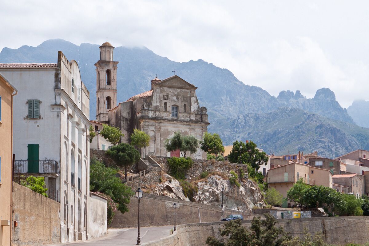 A historic building with a bell tower, situated on a hillside with a mountain backdrop.