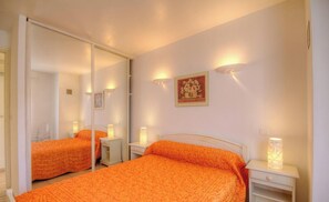Ein Schlafzimmer mit zwei Betten, einem großen Spiegel, Nachttischlampen und einem gerahmten Bild an der Wand.
