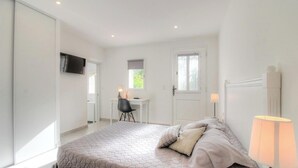 Un dormitorio con cama, escritorio, silla, televisor y lámpara.