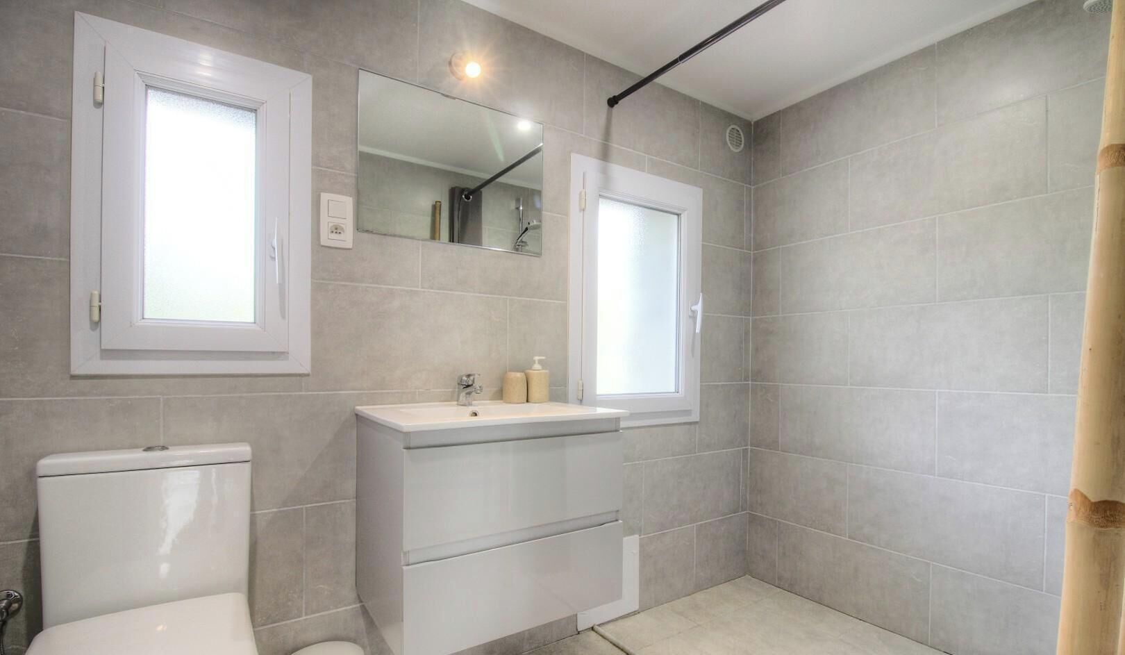 A bathroom with a toilet, sink, mirror, and window.