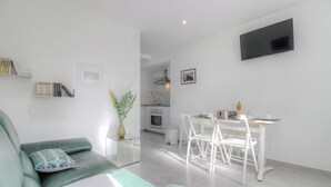 Una sala de estar moderna con un sofá, una mesita con un florero, un comedor con sillas, una cocina al fondo y un televisor montado en la pared.