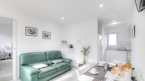 Una sala de estar moderna con un sofá verde, una mesa de comedor con alimentos para el desayuno y una cocina visible al fondo.