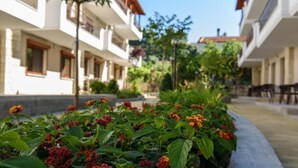 A courtyard with a flower bed, buildings with balconies, and a clear sky.