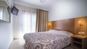 A hotel room with a large bed, a TV mounted on the wall, a nightstand, and a wooden headboard.