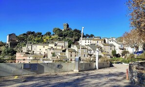 Un village perché sur une colline, avec des bâtiments historiques en pierre, une tour imposante et un espace de stationnement agrémenté d’un panneau indiquant que les places sont réservées aux résidents.