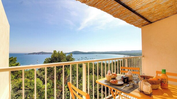 Un balcón con una mesa dispuesta para el desayuno, con vistas a un cuerpo de agua y vegetación.