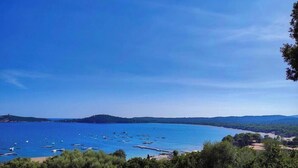 Vista costera con barcos, cielo despejado y colinas a lo lejos.