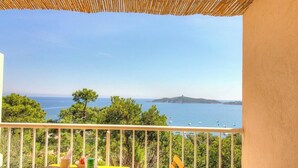 Un balcón con vistas al mar, árboles y una isla distante.