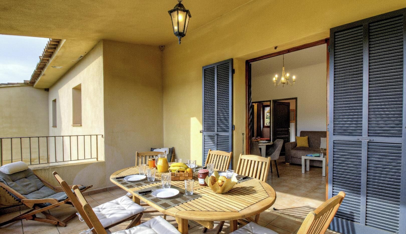 A sunlit patio with a round wooden table set for breakfast, surrounded by wicker chairs.
