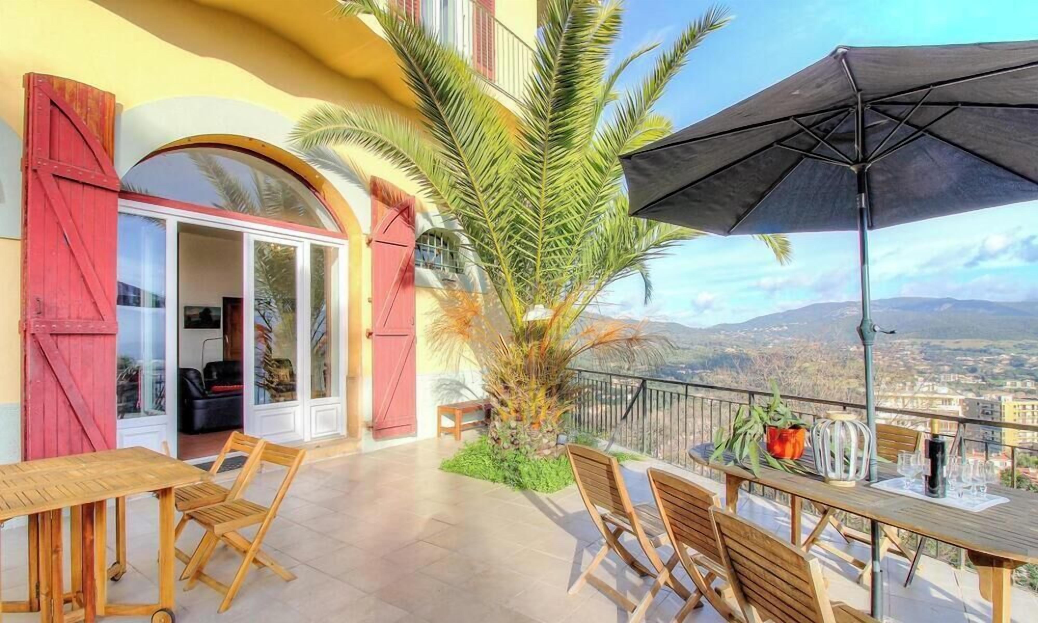 A balcony with a table and chairs, a palm tree, and a view of the city.