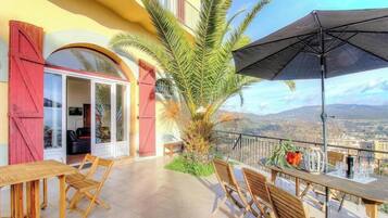 A balcony with a table and chairs, a palm tree, and a view of the city.