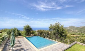 A rectangular swimming pool with a wooden deck, surrounded by greenery and a view of the sea and hills. - Villa Apolisa - MONTICELLO (MONTICELLO)