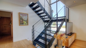 Een modern interieur met een trap, een houten deur, een poster en een houten kast met een vaas.