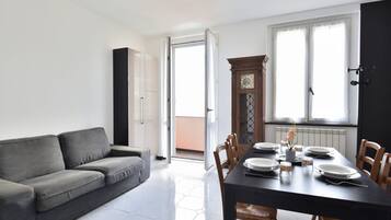 Un soggiorno moderno con un divano grigio, un tavolo da pranzo apparecchiato con piatti e tazze, e un'ampia finestra con tende.